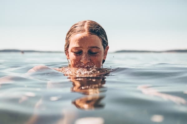 Wild swimming - Teenage girl in the ocean with her head partially out of the water.